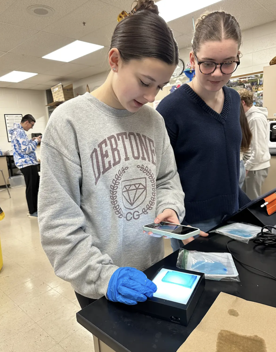 In Danielle Myers AP Biology class, juniors Allison Hopkins and Audrey Johnston place their gel electrophoresis trays onto a transilluminator to examine and photograph the stained gel of lambda DNA. The lab has allowed students to be able to look at DNA fragments and how these fragments cut themselves during gel electrophoresis to base-pair size. "I learned how to stain and rinse gels to look at lambda DNA and measure its migration distance for our Restriction Enzyme Lab," Hopkins said. "It was interesting to see the relationship between the molecular weight of DNA fragments and its mobility on the gels."